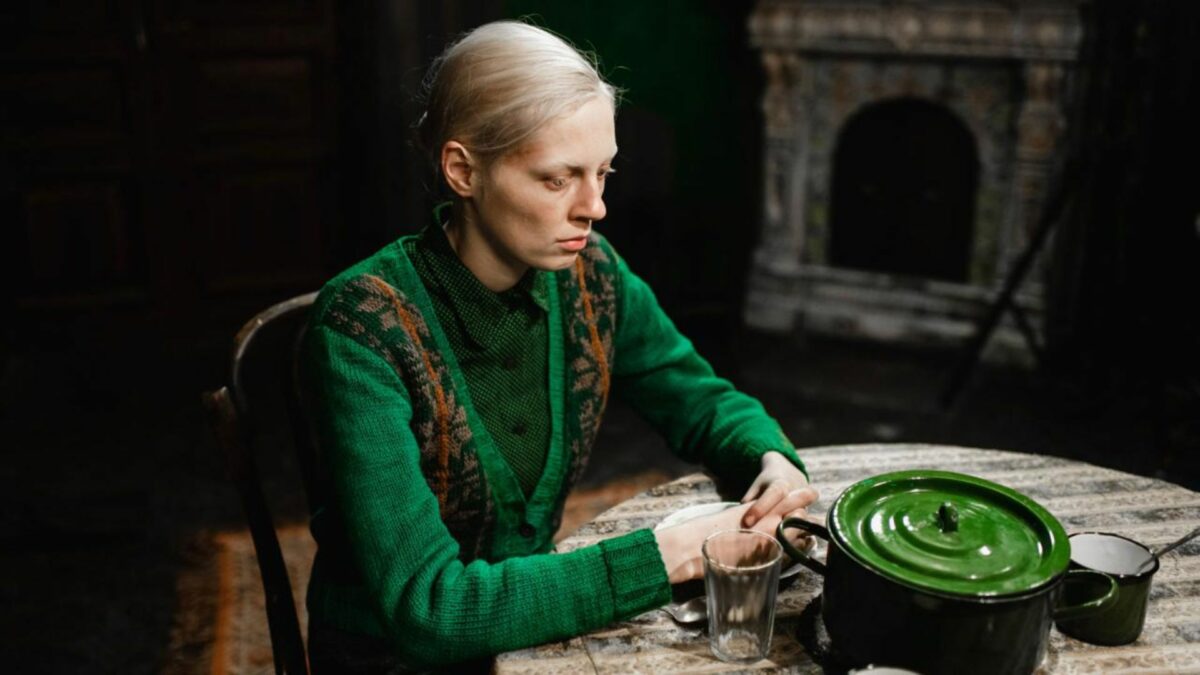 Kadr w ciemnym pomieszczeniu, dziewczyna siedzi przy stole.