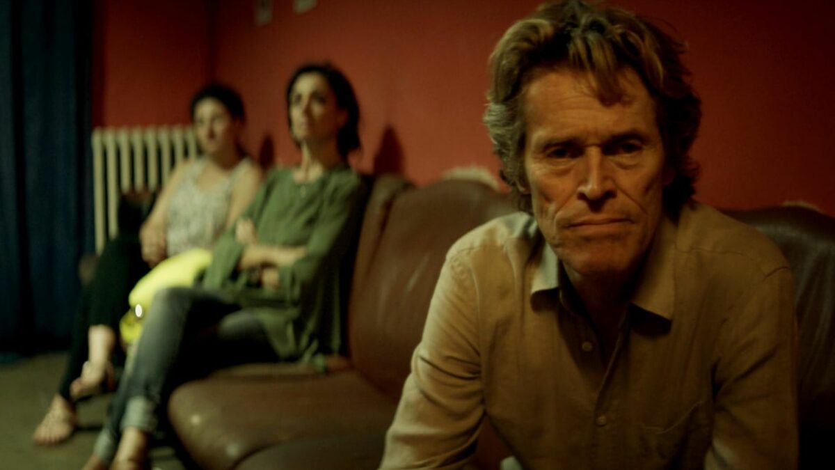 Mężczyzna siedzący na sofie, za nim dwie kobiety.