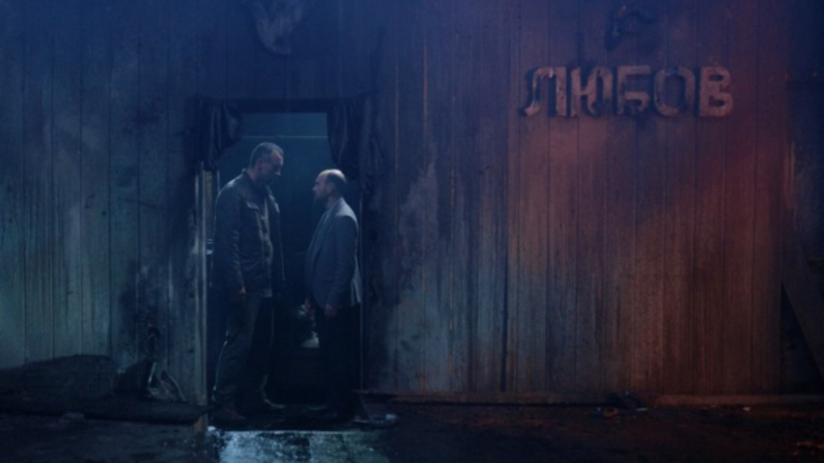 Główny bohater z innym mężczyzną na tle ciemnego konteneru.