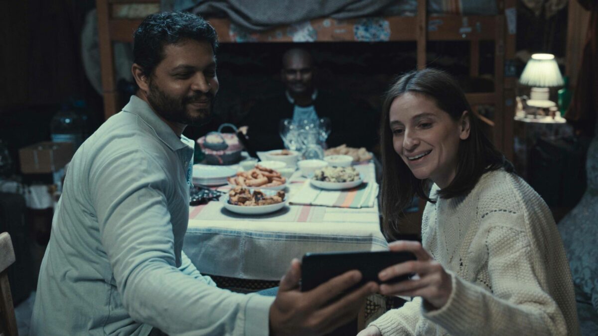 Scena przy stole, mężczyzna pokazuje coś kobiecie na telefonie komórkowym.