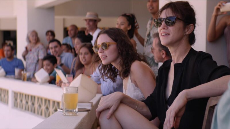 Dwie młode kobiety a za nimi większy tłum wyglądający z balkonu.