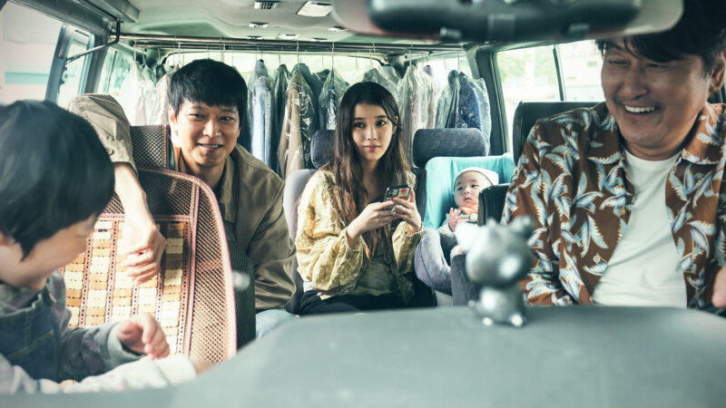 Kadr przedstawia jazdę w dużym samochodzie grupy ludzi którą można wziąć za rodzinę.