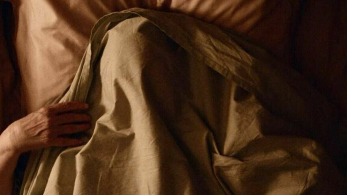 Starsza osoba w łóżku przykrywająca głowę kołdrą.