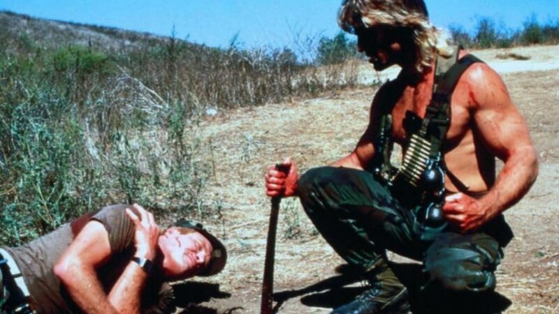 Uzbrojony mężczyzna pochyla się nad swoją ofiarą.