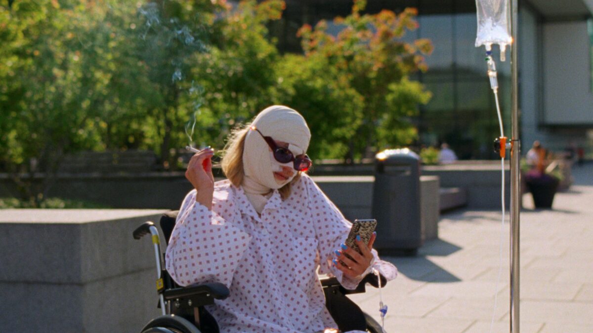 Młoda dziewczyna na wózku inwalidzkim i zabandażowanej twarzy robi sobie selfie.