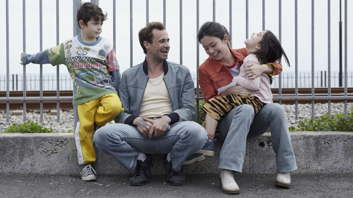 Rodzina, mężczyzna i kobieta z dwójką dzieci przysiadających na krawężniku.