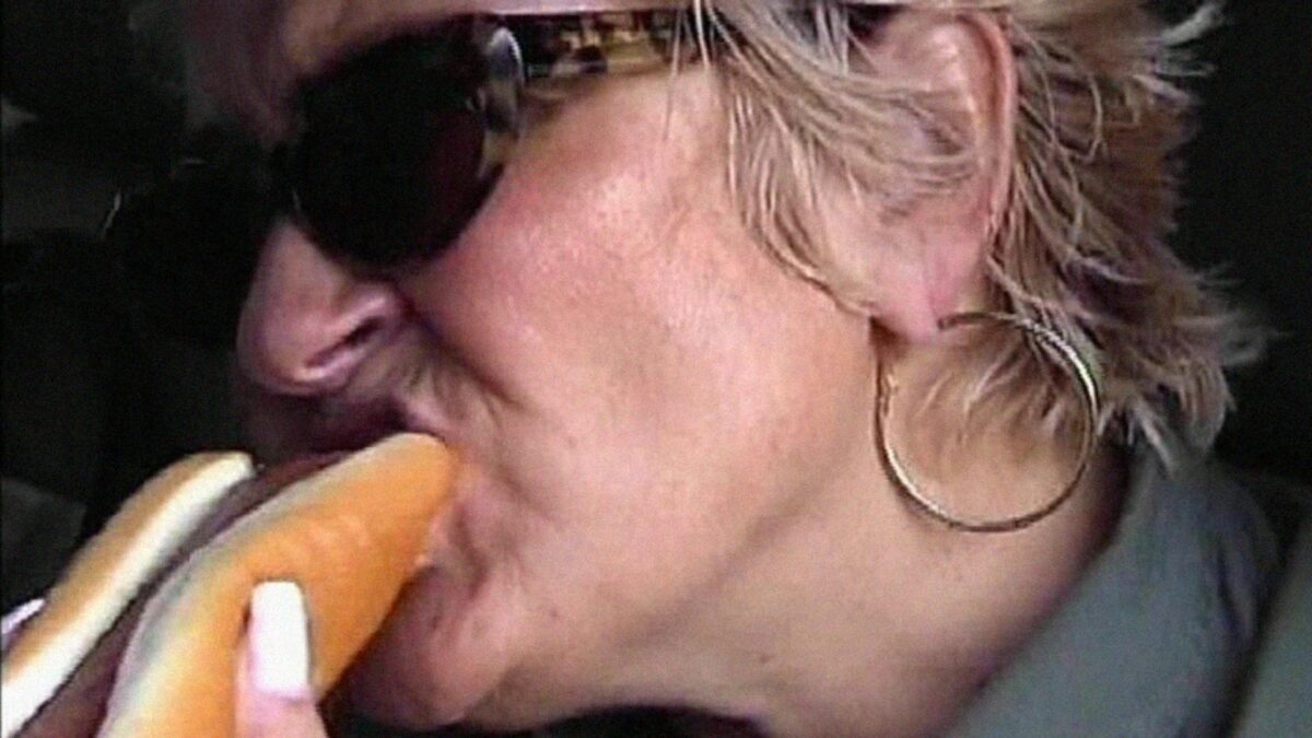 Kobieta w ciemnych okularach zajadająca się hot-dogiem.