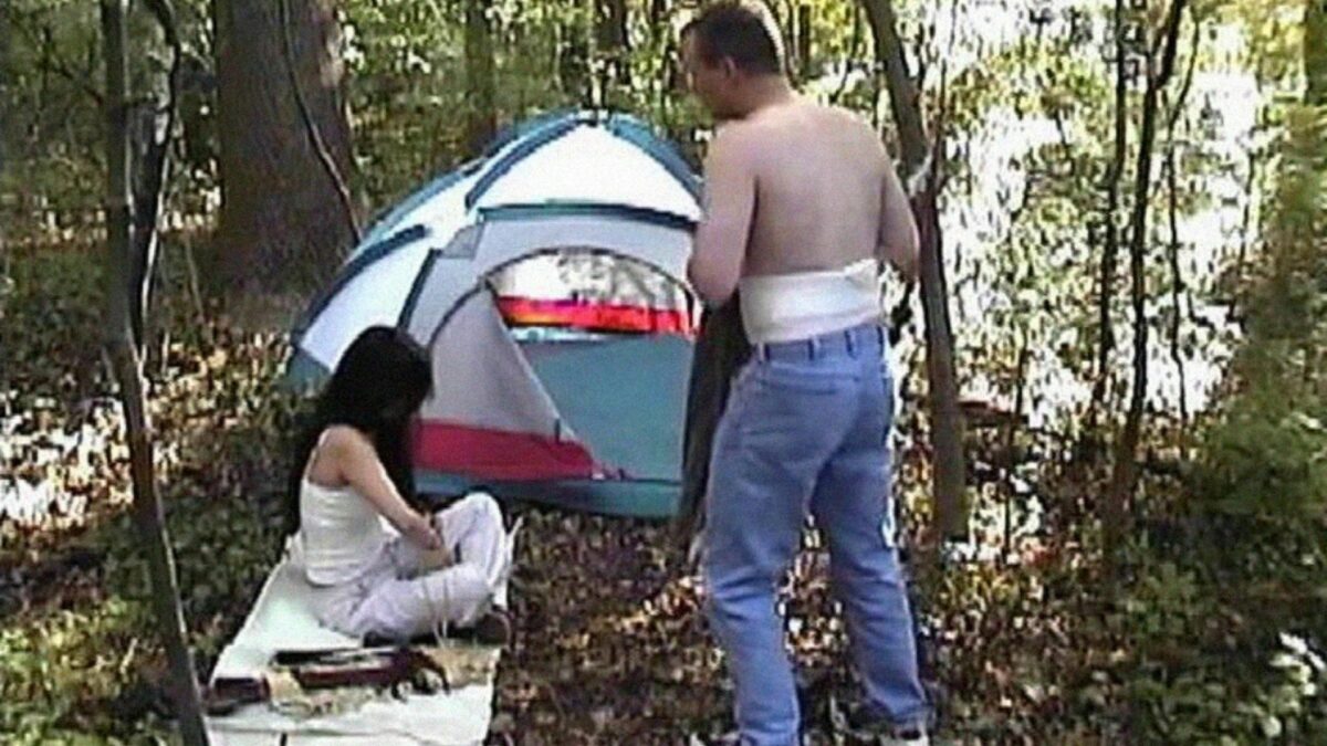 Kobieta i mężczyzna w lesie przed rozstawionym namiotem.