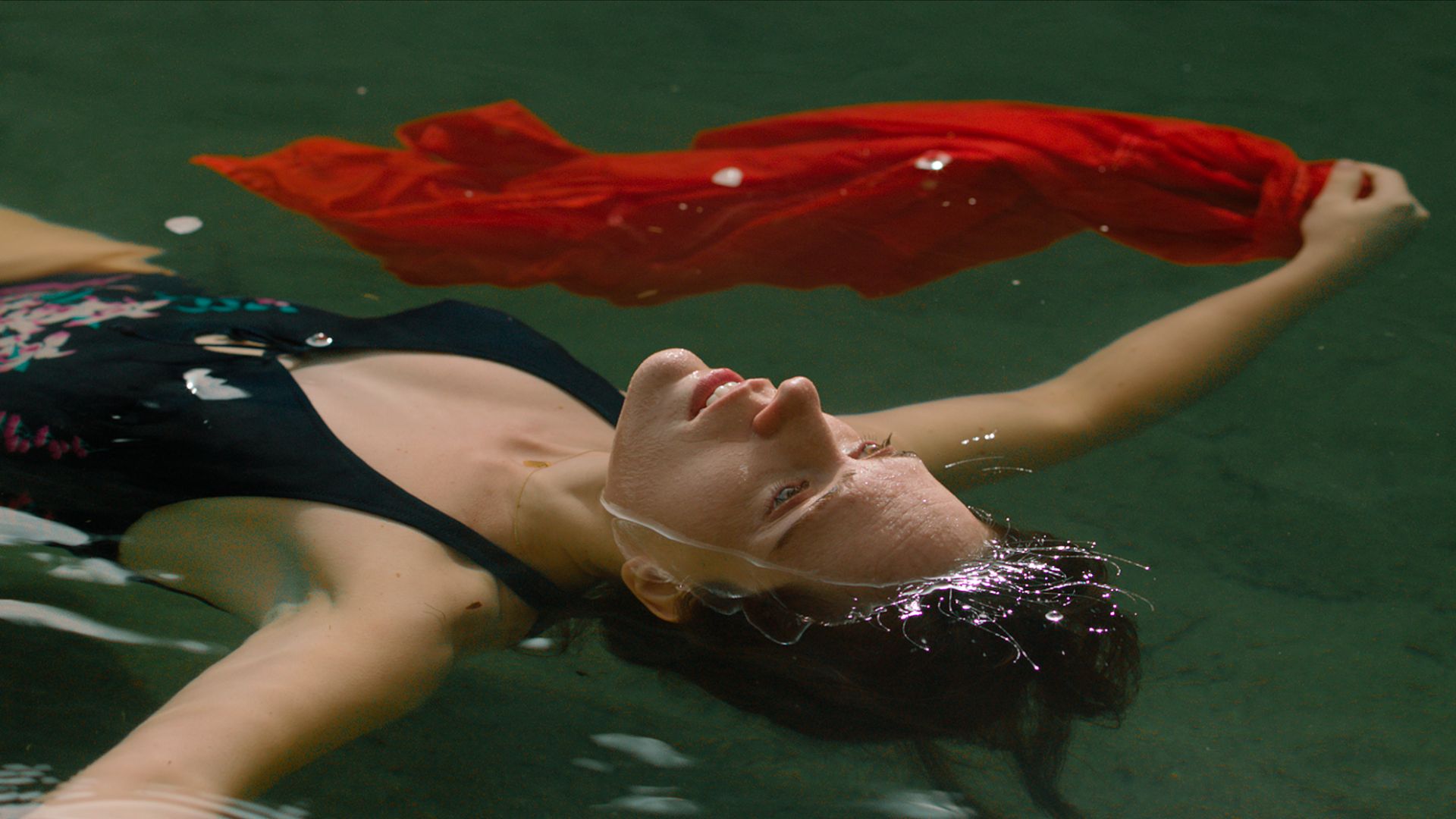 Kobieta w stroju kąpielowym z czerwoną chustą w dłoni, pływająca w basenie