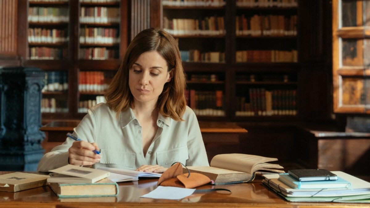 Kobieta przy biurku na tle biblioteczki.