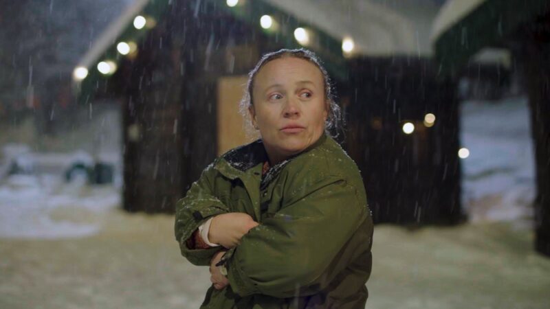 Kobieta okrywająca się kurtką w zimowej aurze.