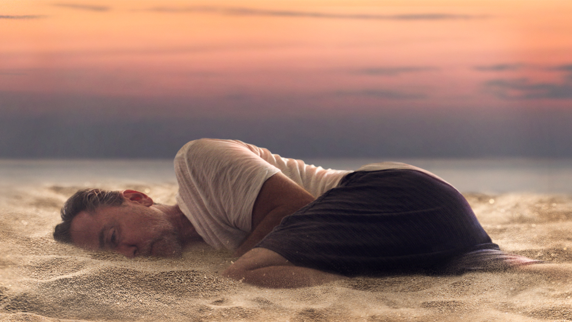 Mężczyzna leżący na plaży w pozycji skulonej, powoli pokryty pokrywa się przez piasek.