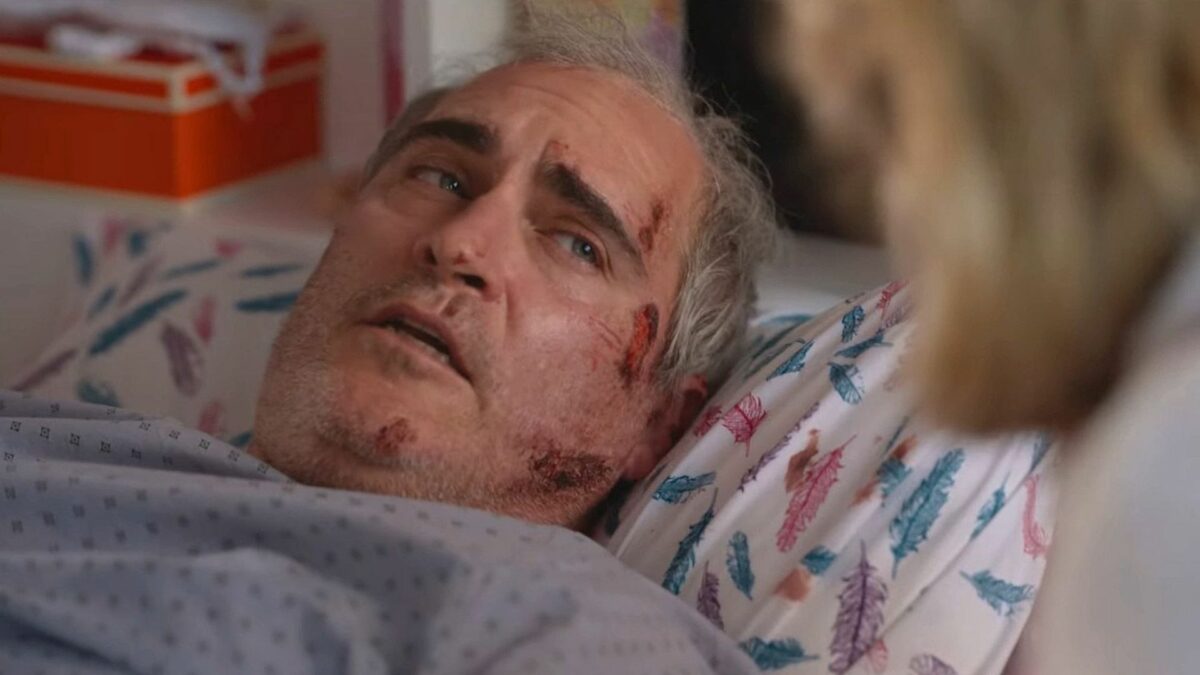 Mężczyzna leżący na łóżku w towarzystwie osoby, która jest mało widoczna na kadrze.