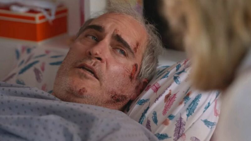 Mężczyzna leżący na łóżku w towarzystwie osoby, która jest mało widoczna na kadrze.