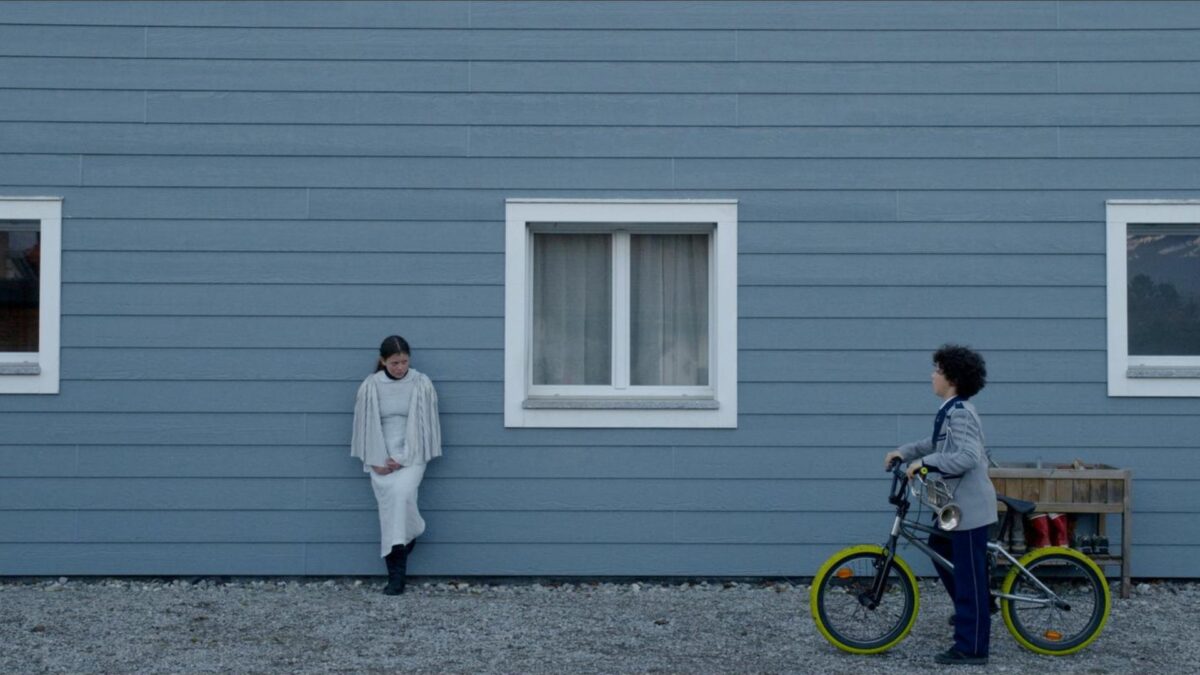 Dziewczynka stojąca pod budynkiem, obok zatrzymuje się chłopiec na rowerze.