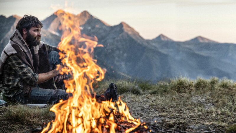 Mężczyzna w górach przy rozpalonym ognisku.