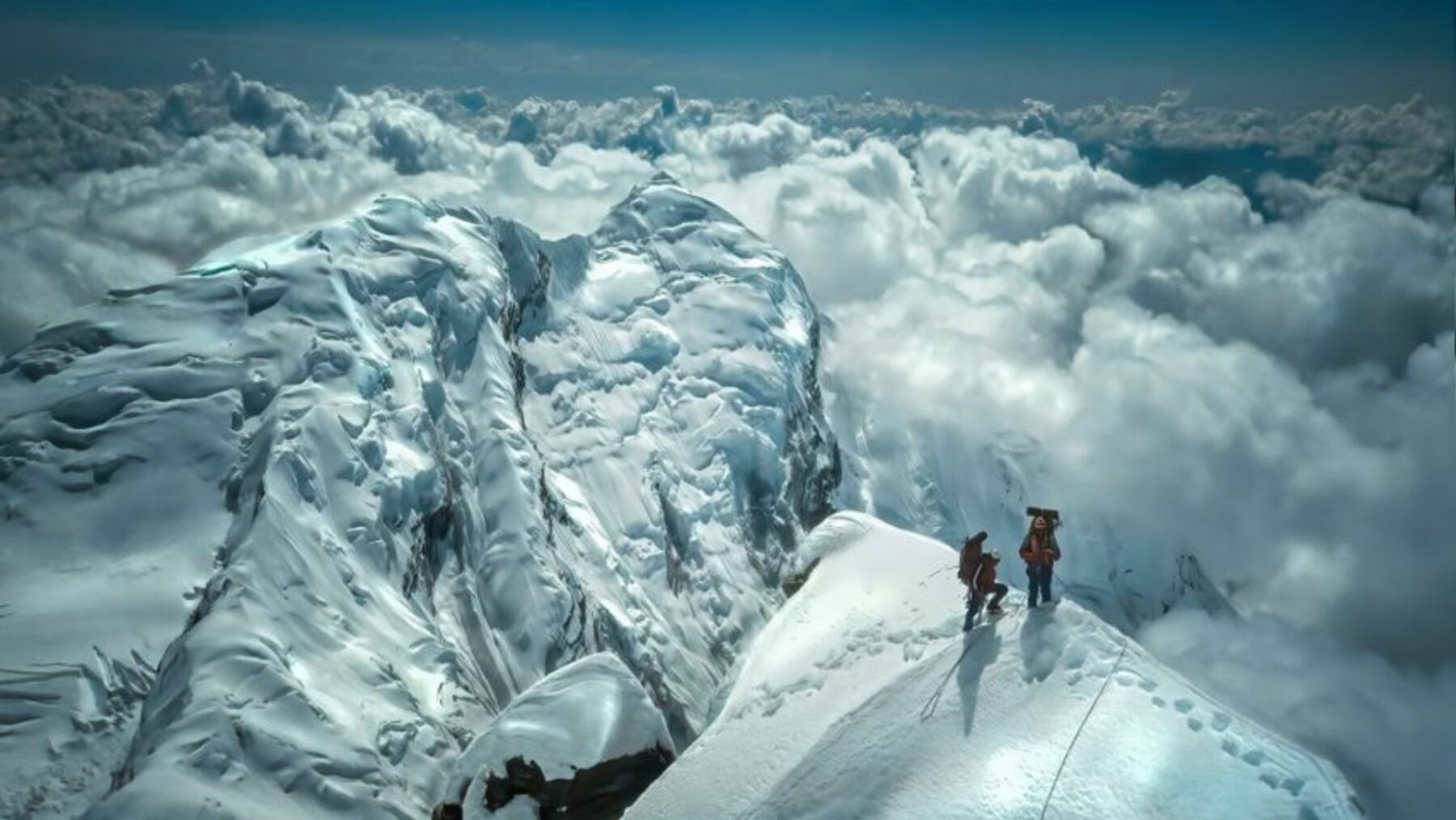 Rozległą panorama górska, w oddali dwie osoby na ośnieżonym szczycie.