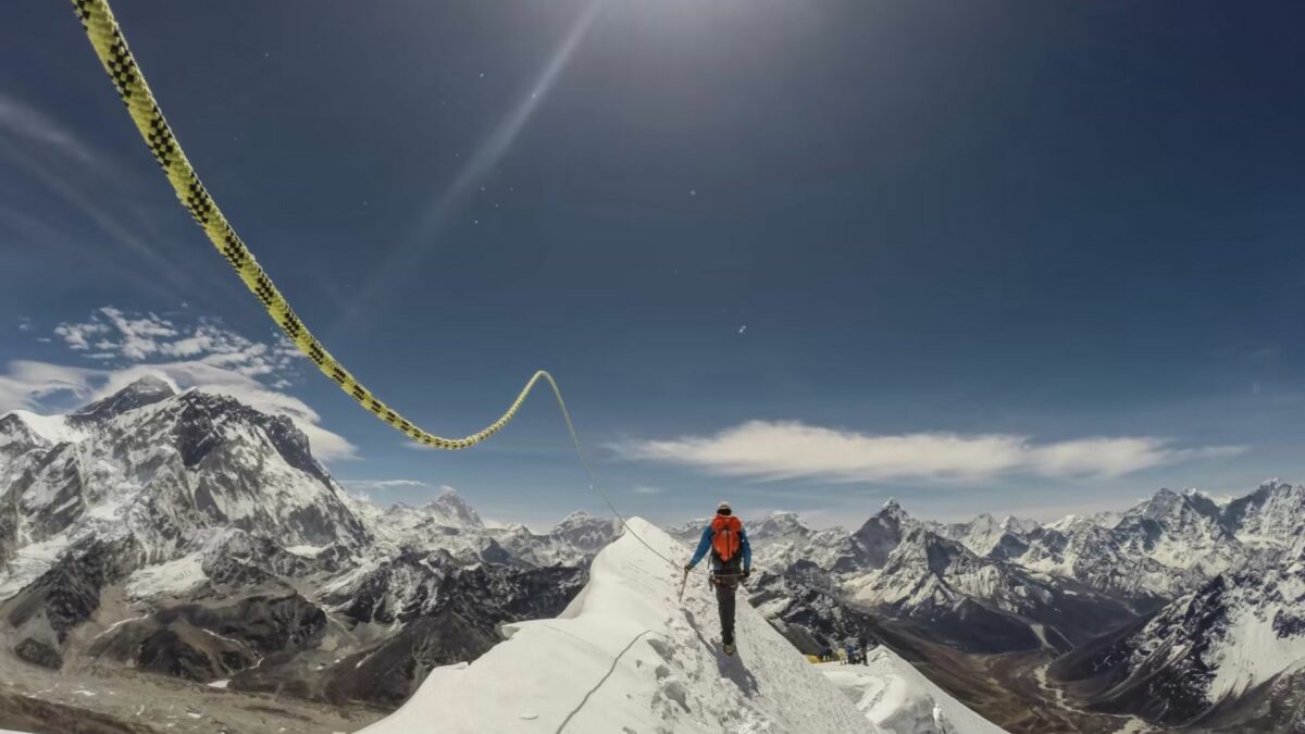 Ośnieżony szczyt górski, w oddali widać osobę zmierzającą na szczyt.