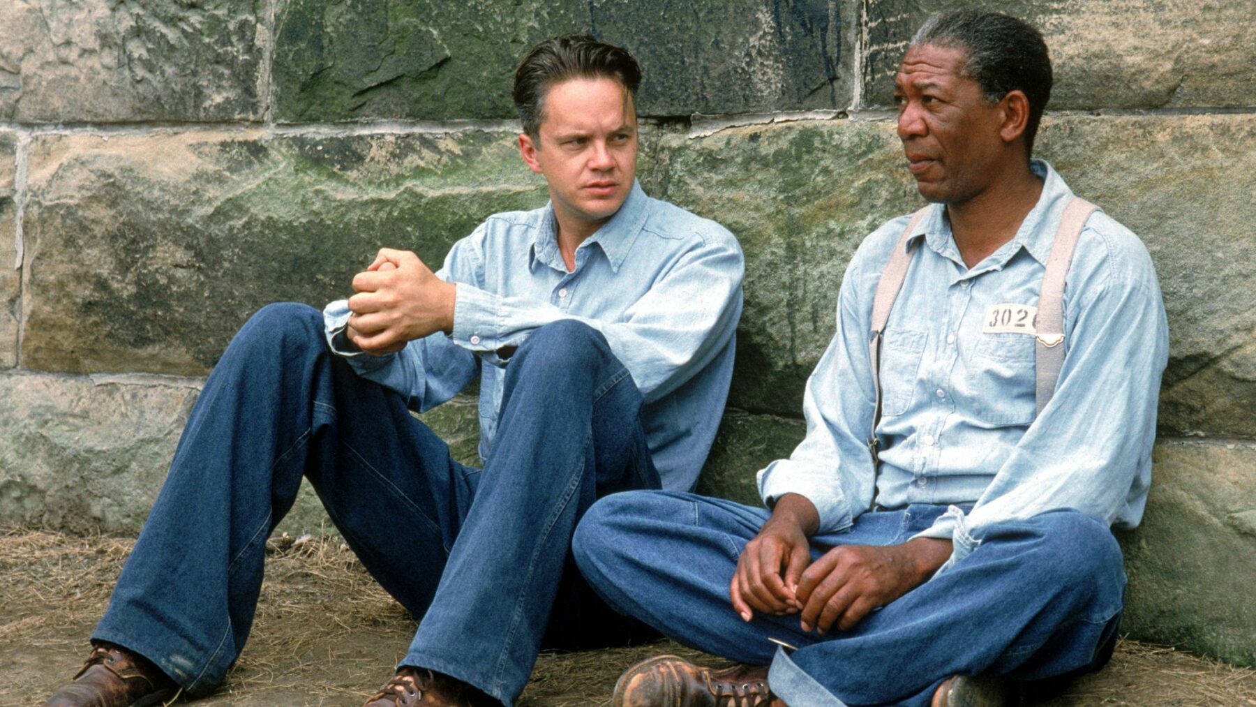 Dwójka więźniów siedzi oparta o murek na spacerniaku.