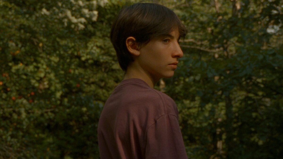 Młody chłopka w lesie, stoi tyłem i odwraca się w do przodu.