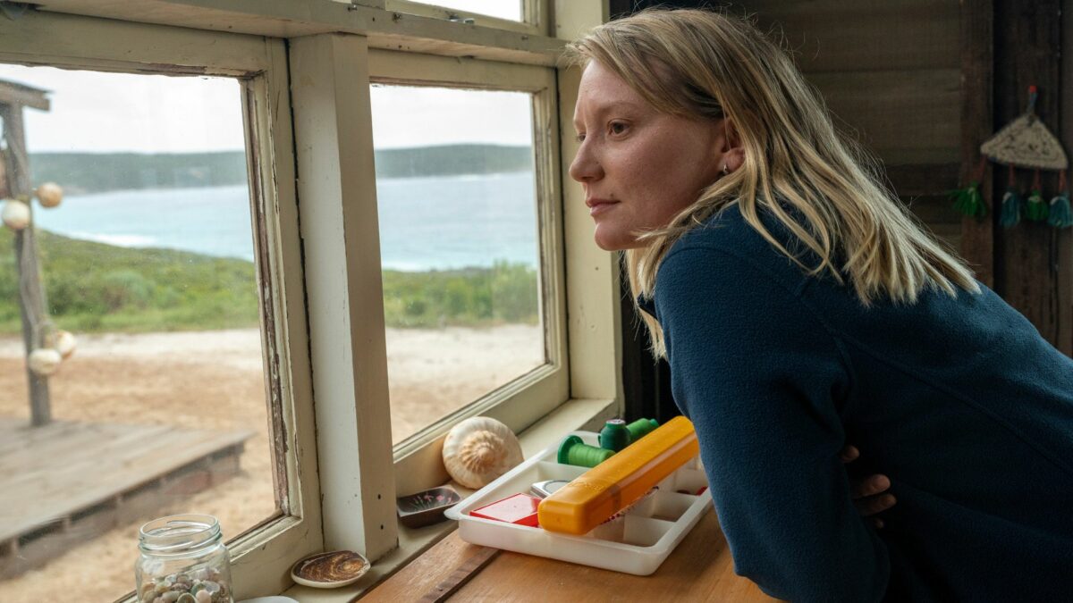 Kobieta wyglądająca przez okno z domu na plażę.