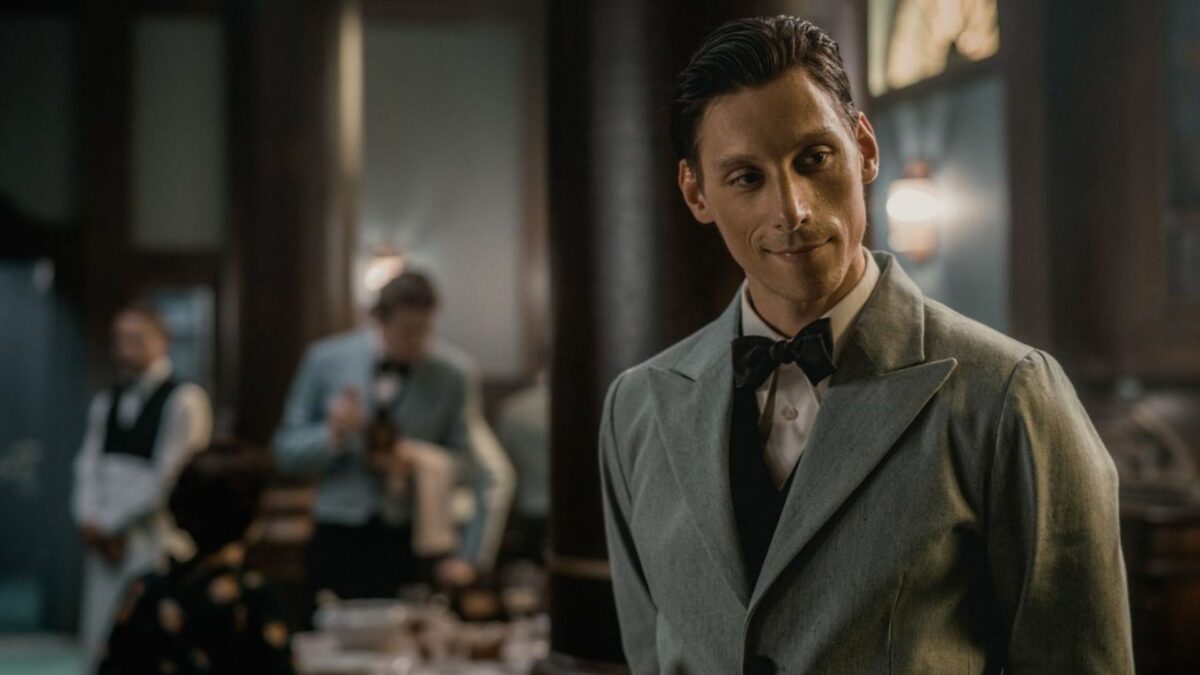 Scena z restauracji, zbilżenie na kelnera w oddali widać inny stolik z gośćmi i obsługą sali.