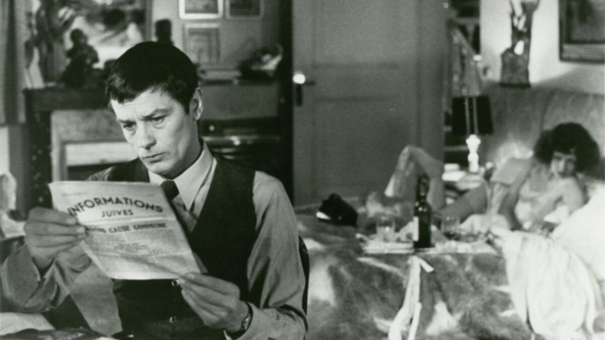 Mężczyzna czytający gazetę, na drugim planie znajduje się kobieta na łóżku, ma wino i kieliszki.