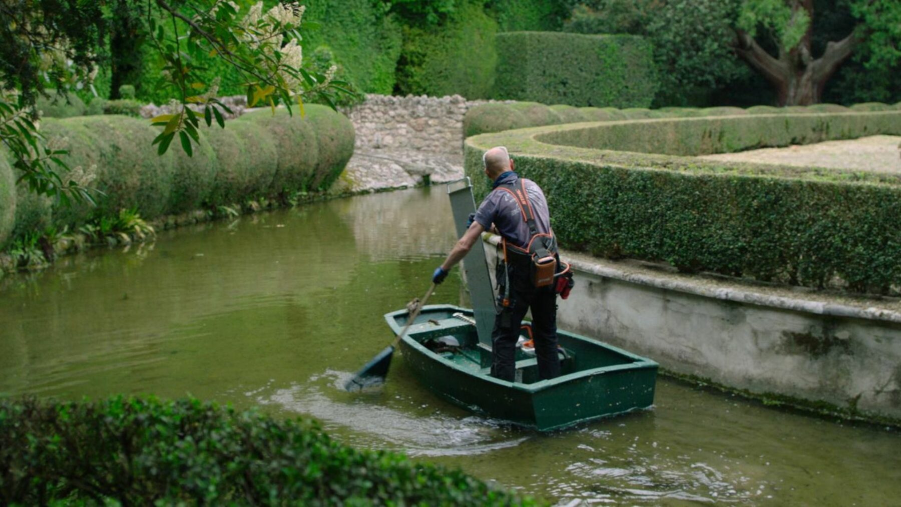 Mężczyzna na łódce w ogrodowym stawie.