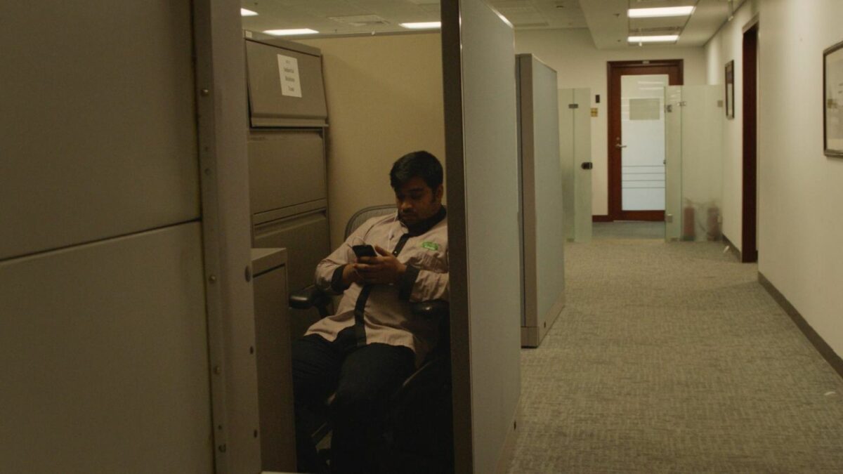 Przestrzeń biurowa, kadr na pracownika siedzącego przy telefonie.