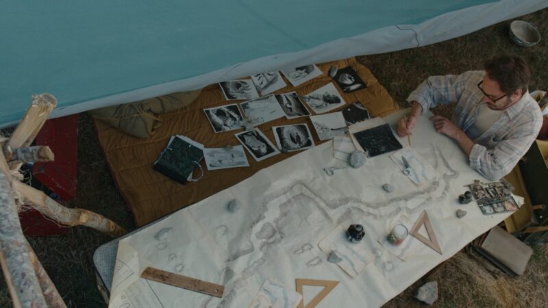 Stanowisko archeologiczne, pracownik przy mapach i innych dokumentach.