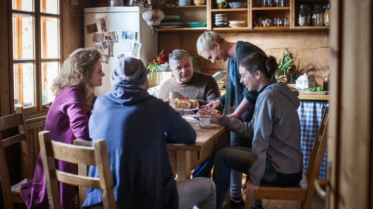 Kadr przy rodzinnym stole, pięcioosobowa rodzinya zasiada [rzy stole z ciastem i kawą.