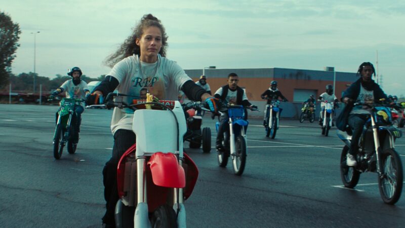 Scena na parkingu, duża grupa motocyklistów wyjeżdża na drogę.