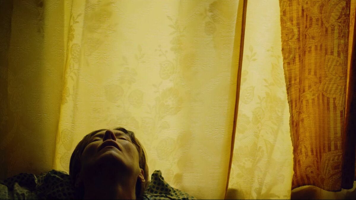 kadr na leżącą kobietę na tle firanek w oknie.