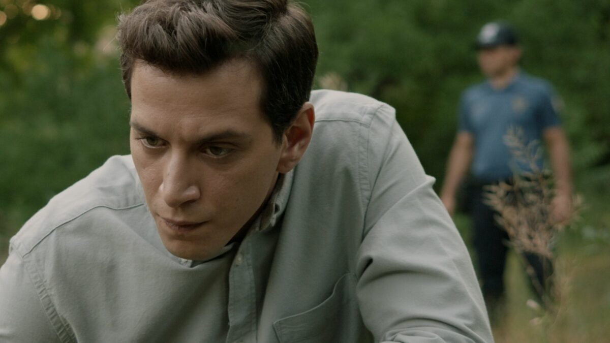 mężczyzna pochylający się do ziemi za nim w tle policjant.