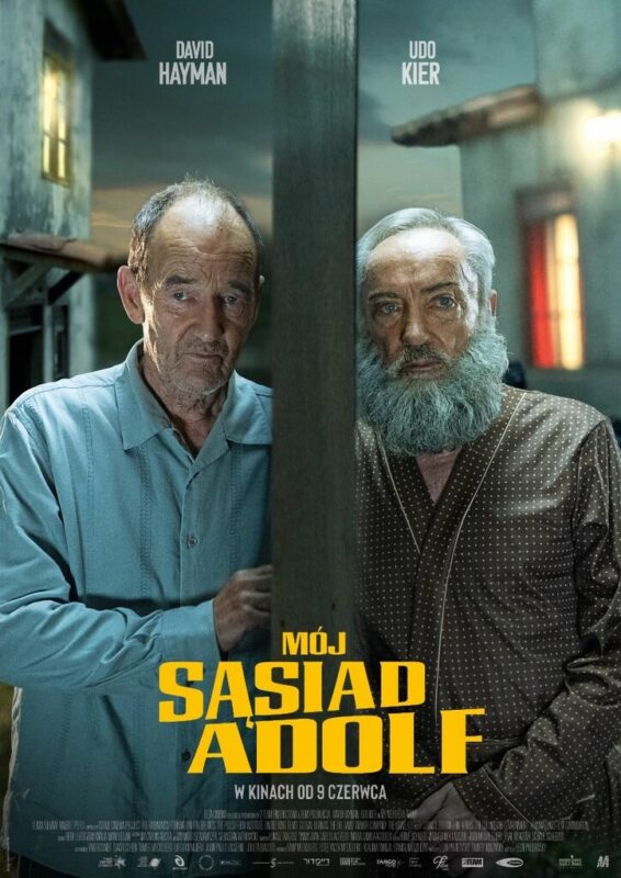 Dwaj mężczyźni ubrani w kolorowe piżamy przykładają uszy do drzwi. Znajdują się po przeciwległych stronach, nadsłuchują siebie nawzajem, prawdopodobnie dopiero co zerwali się z łóżek