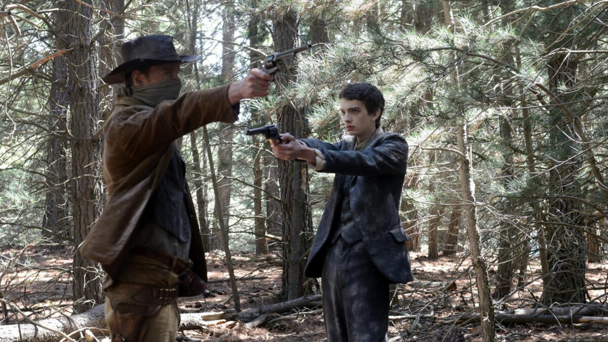 Zamaskowany przestępca celuje do kogoś z broni, jego na muszce ma młody chłopak.