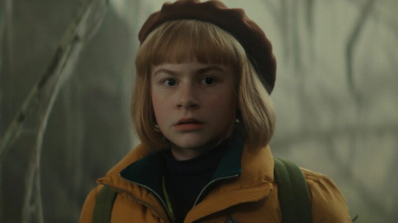 Zbliżenie na dziewczynkę w berecie w mrocznym lesie.