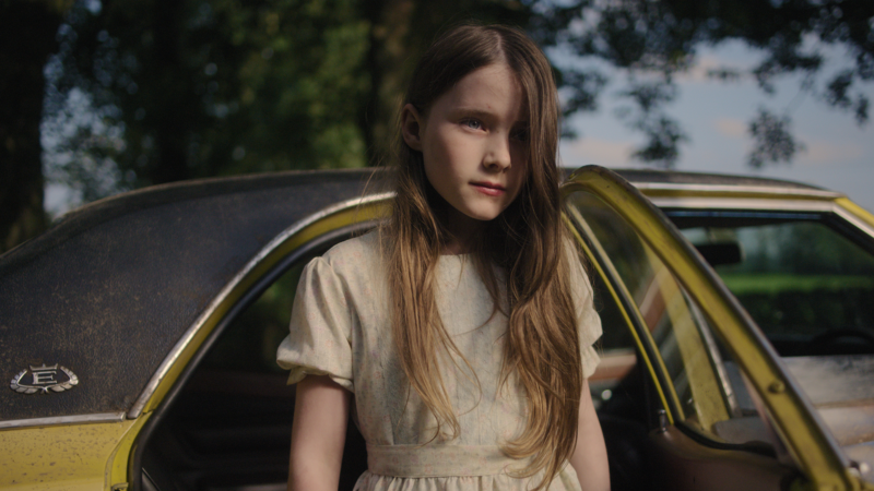 Mała dziewczynka przy żółtym samochodzie.