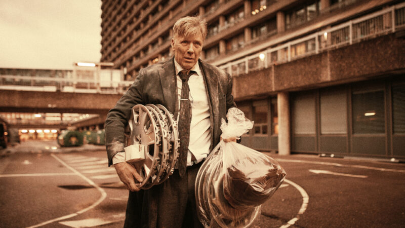 Mężczyzna z rolkami filmowymi przed gmachem szpitala.