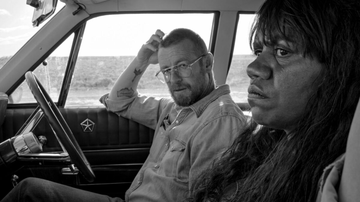 Kadr z przednich siedzeń samochodu, kierowca rozmawia z kobietą.