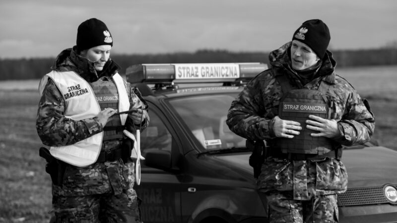 Dwóch pracowników straży granicznej na tle samochodu.