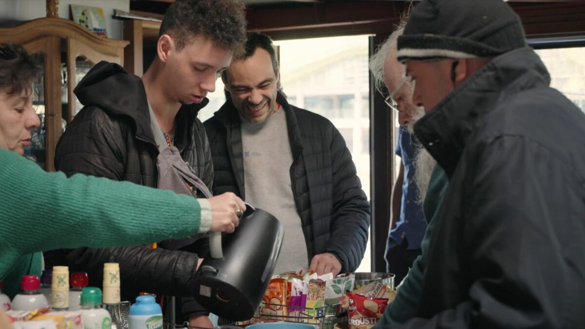 Kadr grupy ludzi częstujących się herbatą.