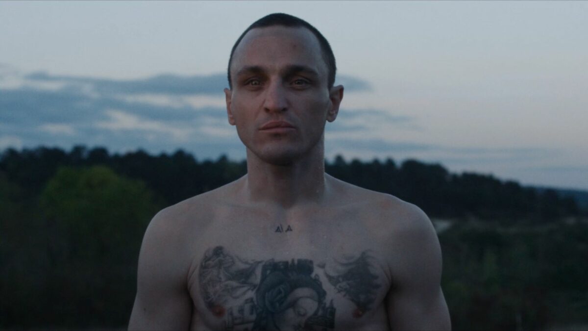 Kadr z mężczyzną z dużym tatuażem na klatce piersiowej.