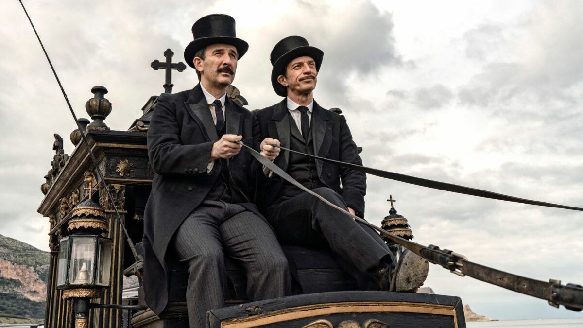 Dwoje Panów w kapeluszach podczas jazdy dorożką.