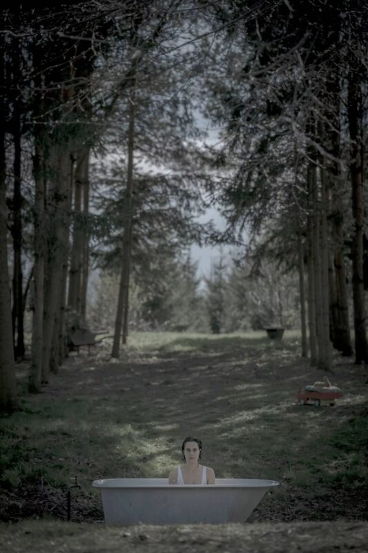 Plakat przedstawia kobietę w wannie w samym środku lasu.