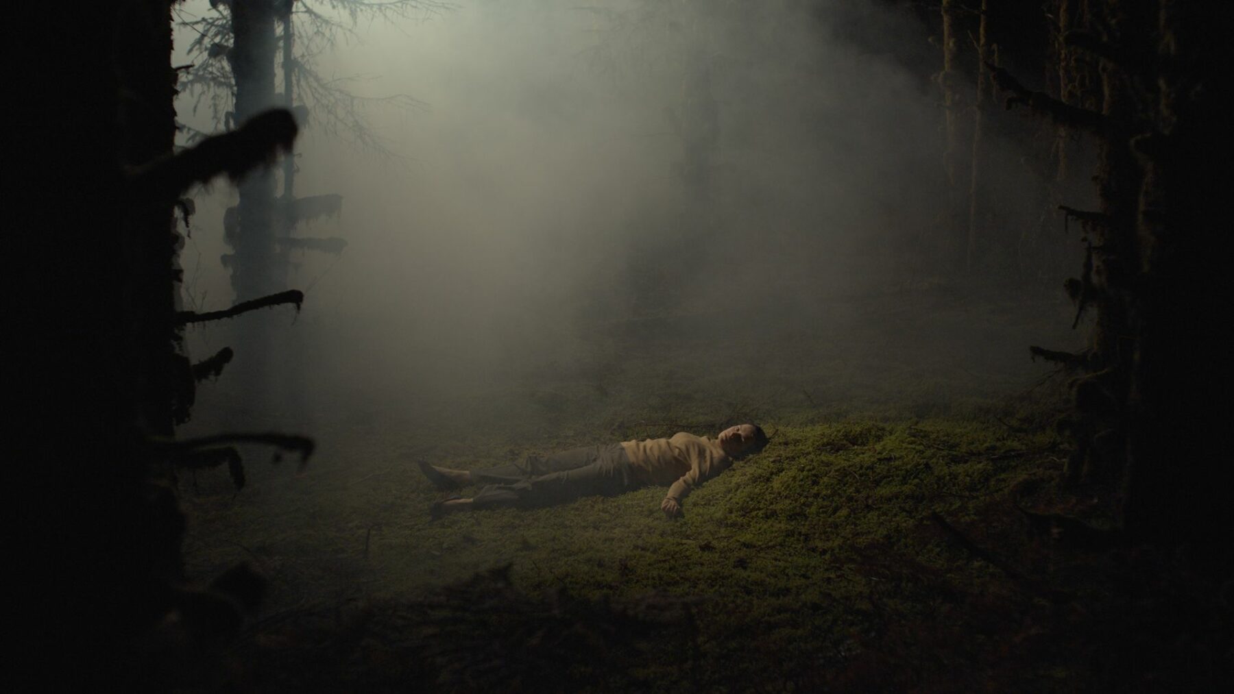 Kadr przedstawiający leżącą kobietę w lesie.