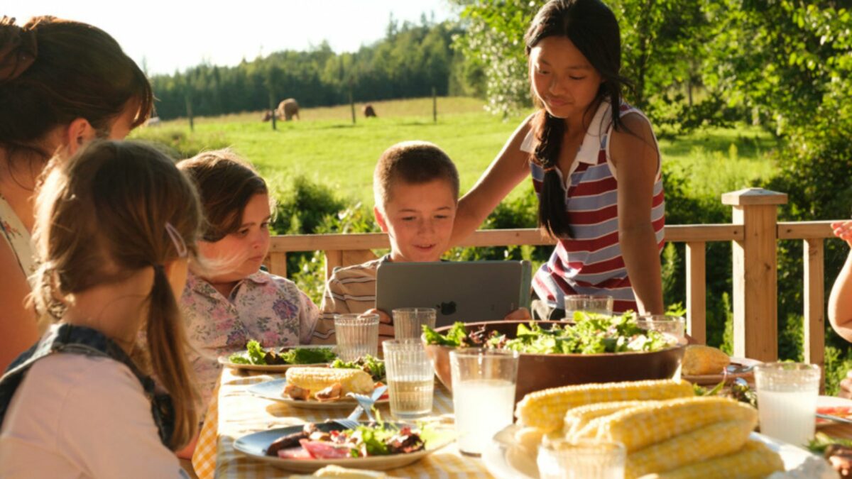 Grupa dzieci z dorosła kobietą przeglądających materiały na tablecie.
