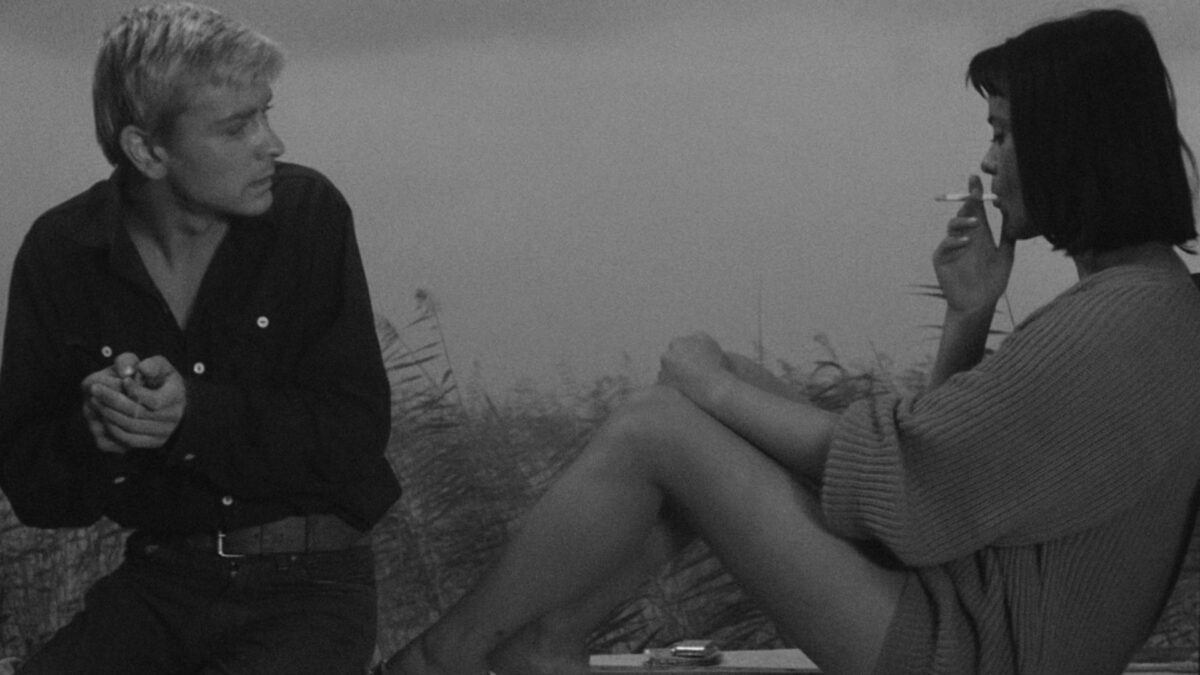 Młoda dziewczyna pali papierosa w towarzystwie mężczyzny.