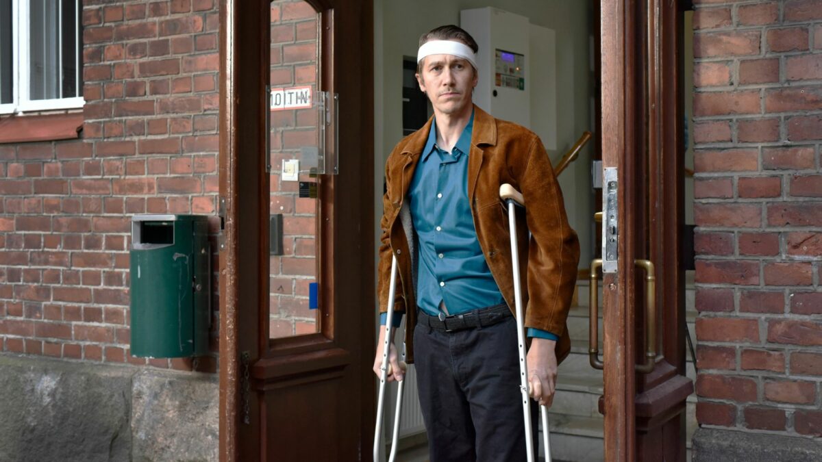 Mężczyzna w bandażach i o kulach wychodzi z zakłądu pracy.