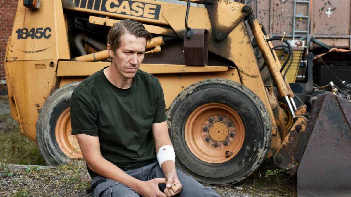 Pracownik fizyczny siedzący obok koparki.